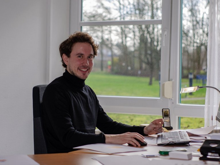 Quartiersmanager Frederik Lauwen am Schreibtisch sitzend lächelt er dem Betrachter zu